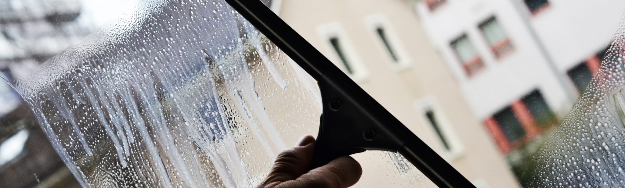 Fensterabzieher auf nassem Glas, dahinter eine Häuserfassade