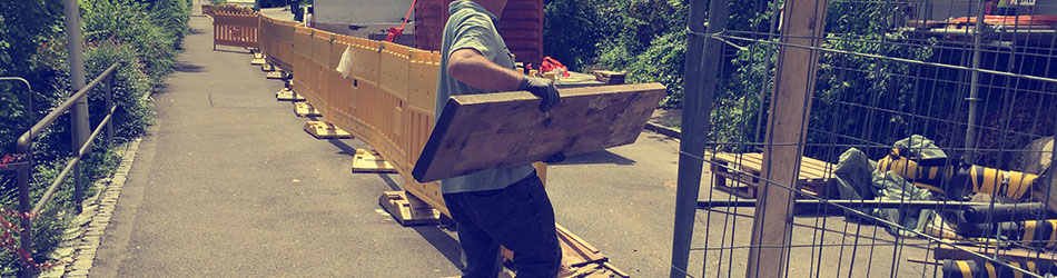 Mitarbeiter trägt Holzbretter über einen Weg