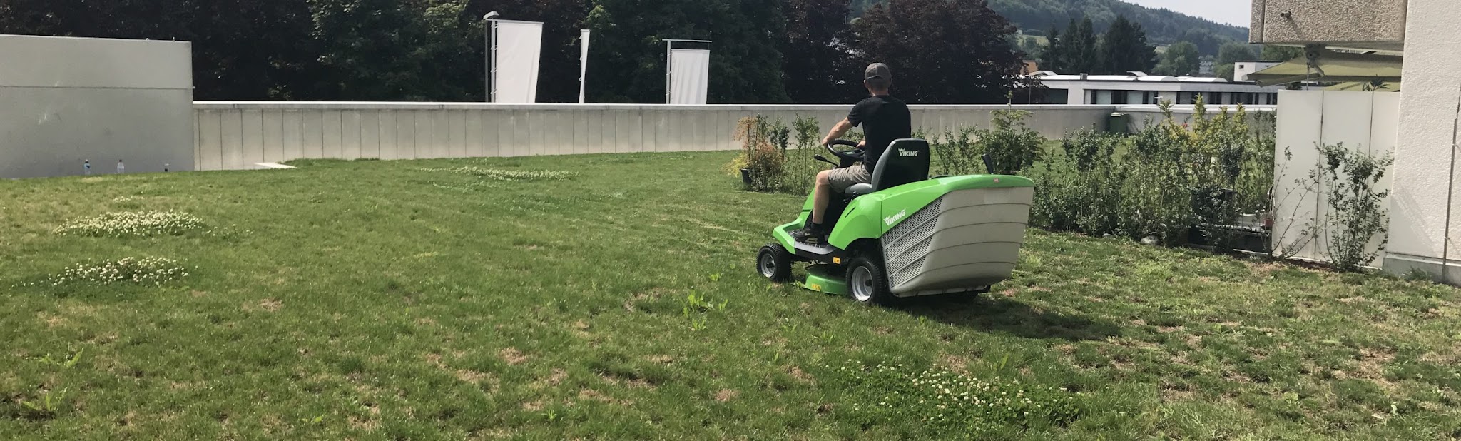 Mitarbeiter auf einem grünen Aufsitzmäher auf einer Rasenfläche